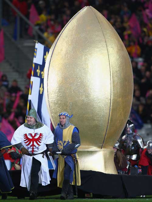 Medieval-costumed men lead pose next to a giant golden rugby ball 