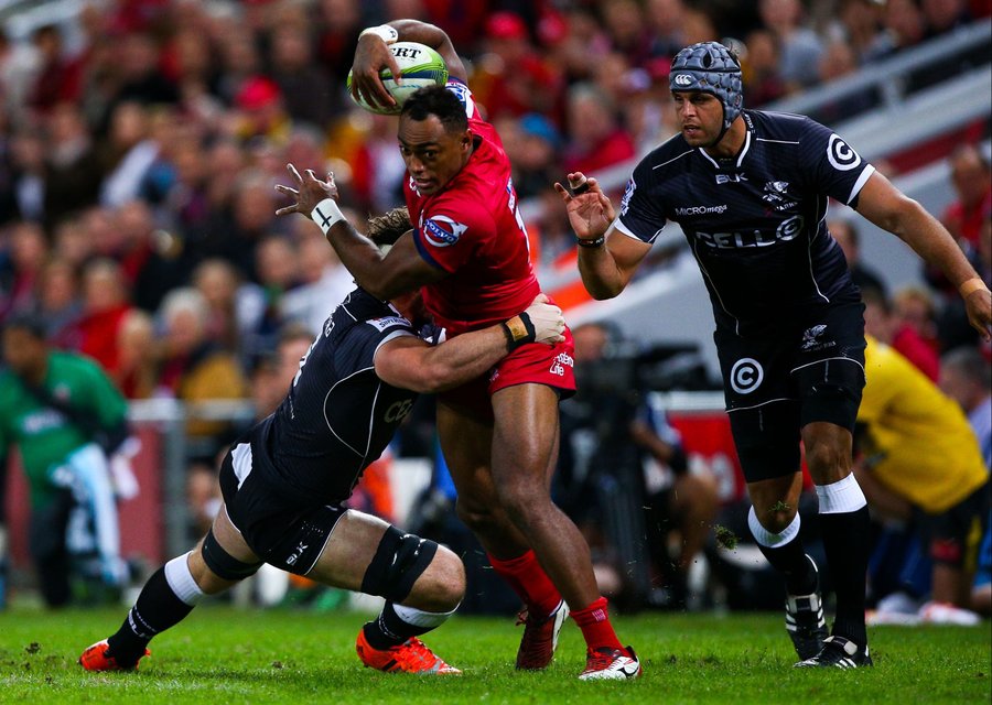 Reds player Chris Kuridrani (C) is tackled by Sharks player Marcell Coetzee